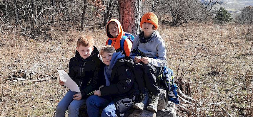 Kinder sitzen auf Holzstapel.