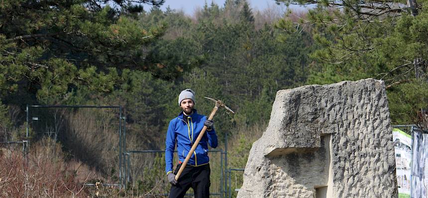 Mensch mit Krampen neben Steinskulptur