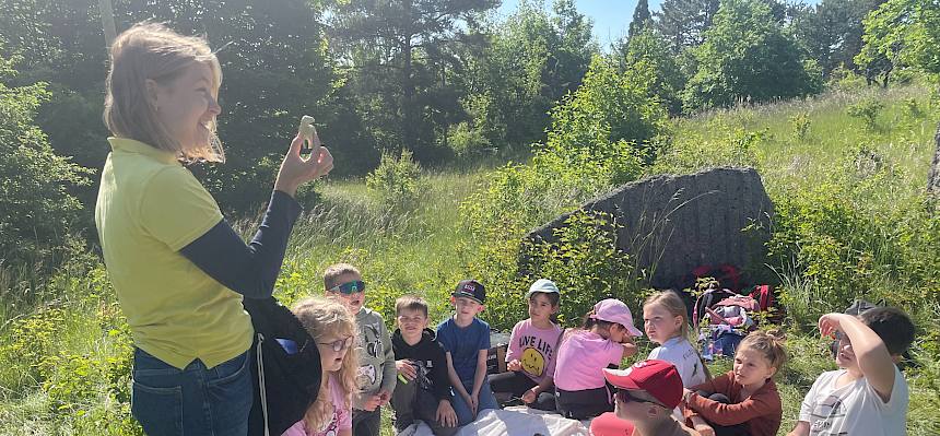 Kinder sitzen im Kreis, Frau zeigt etwas