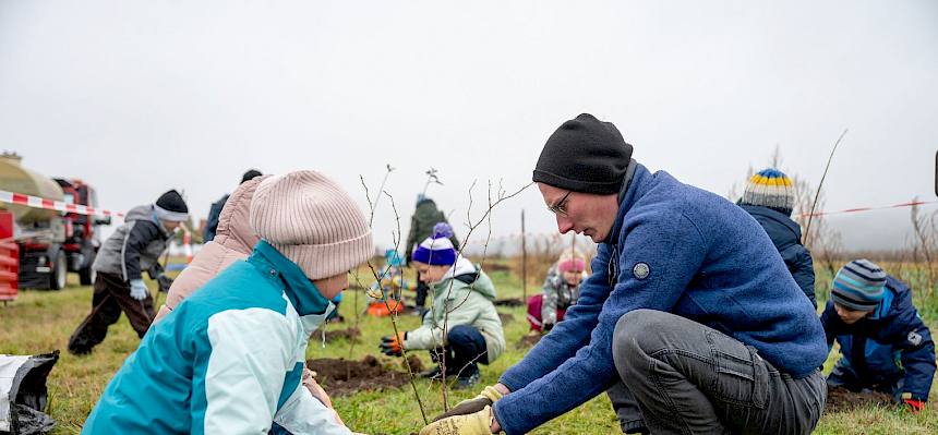 Praktikant hilft Kindern beim Pflanzen von Heckensträuchern